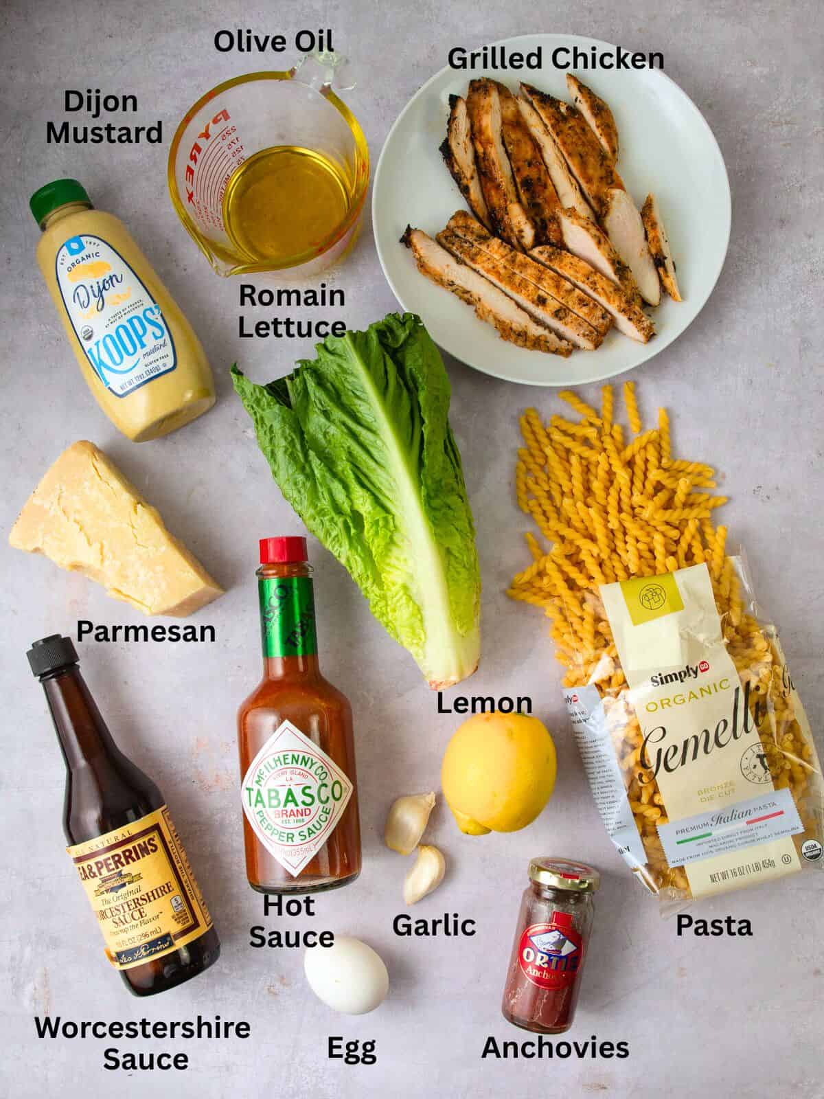 Ingredients for caesar pasta salad including grilled chicken, romaine lettuce, lemon, garlic and olive oil.