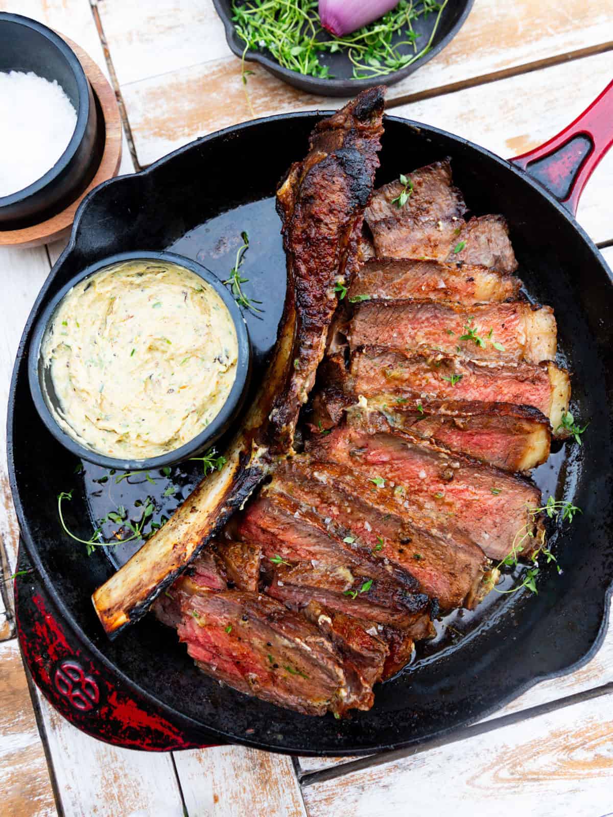Serve the tomahawk steak with charred shallot compound butter and garnish with salt and thyme.