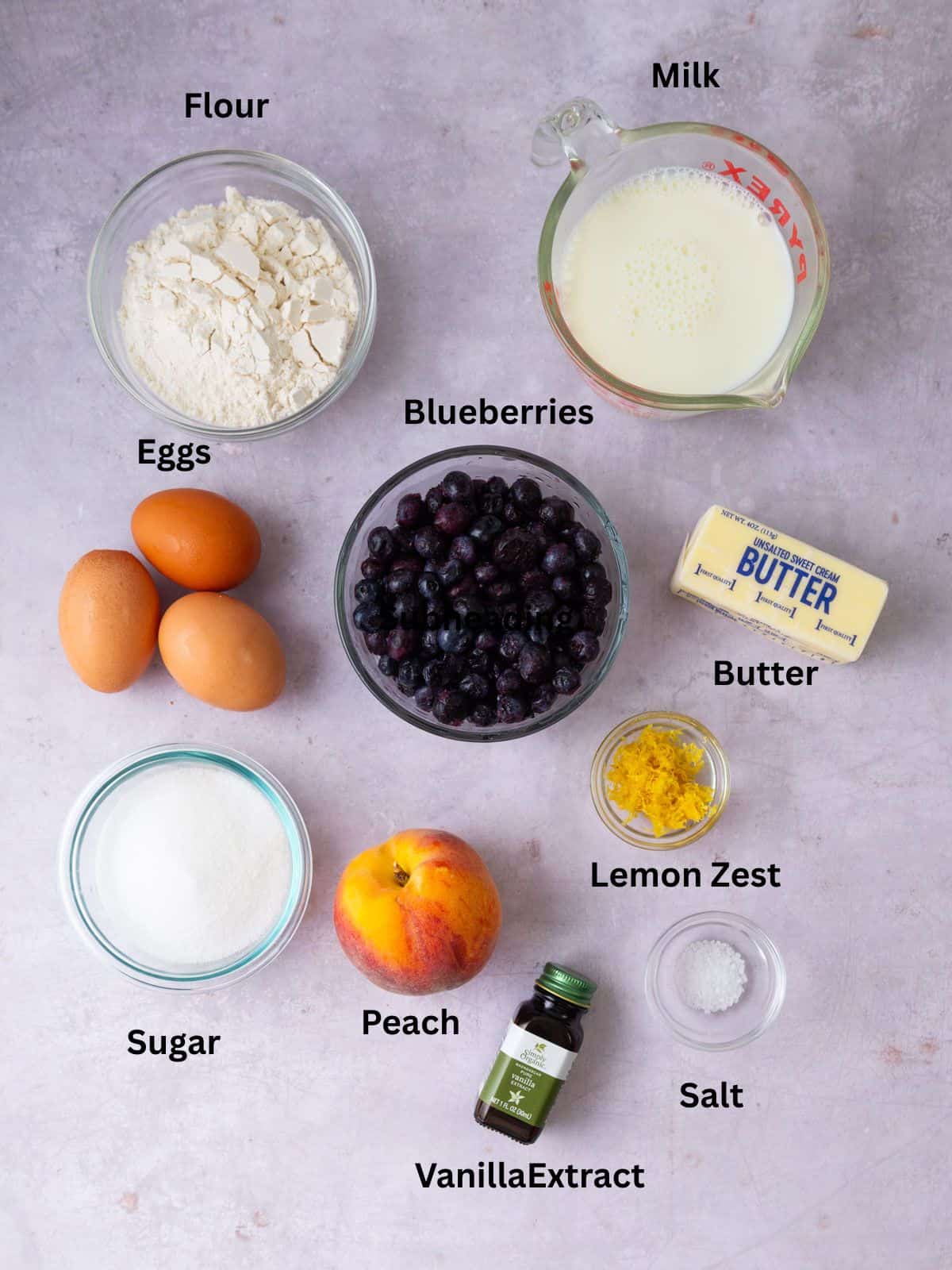 Ingredients for peach and blueberry clafoutis including flour, sugar, butter, vanilla extract and lemon zest.