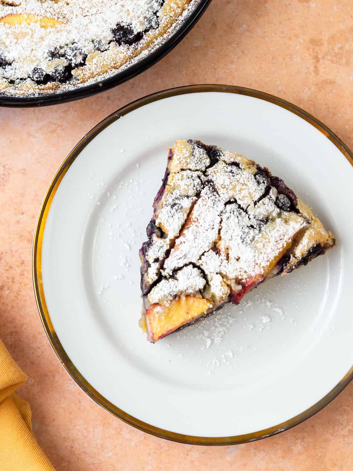 Cut a slice of the peach and blueberry clafoutis and dust with powdered sugar.
