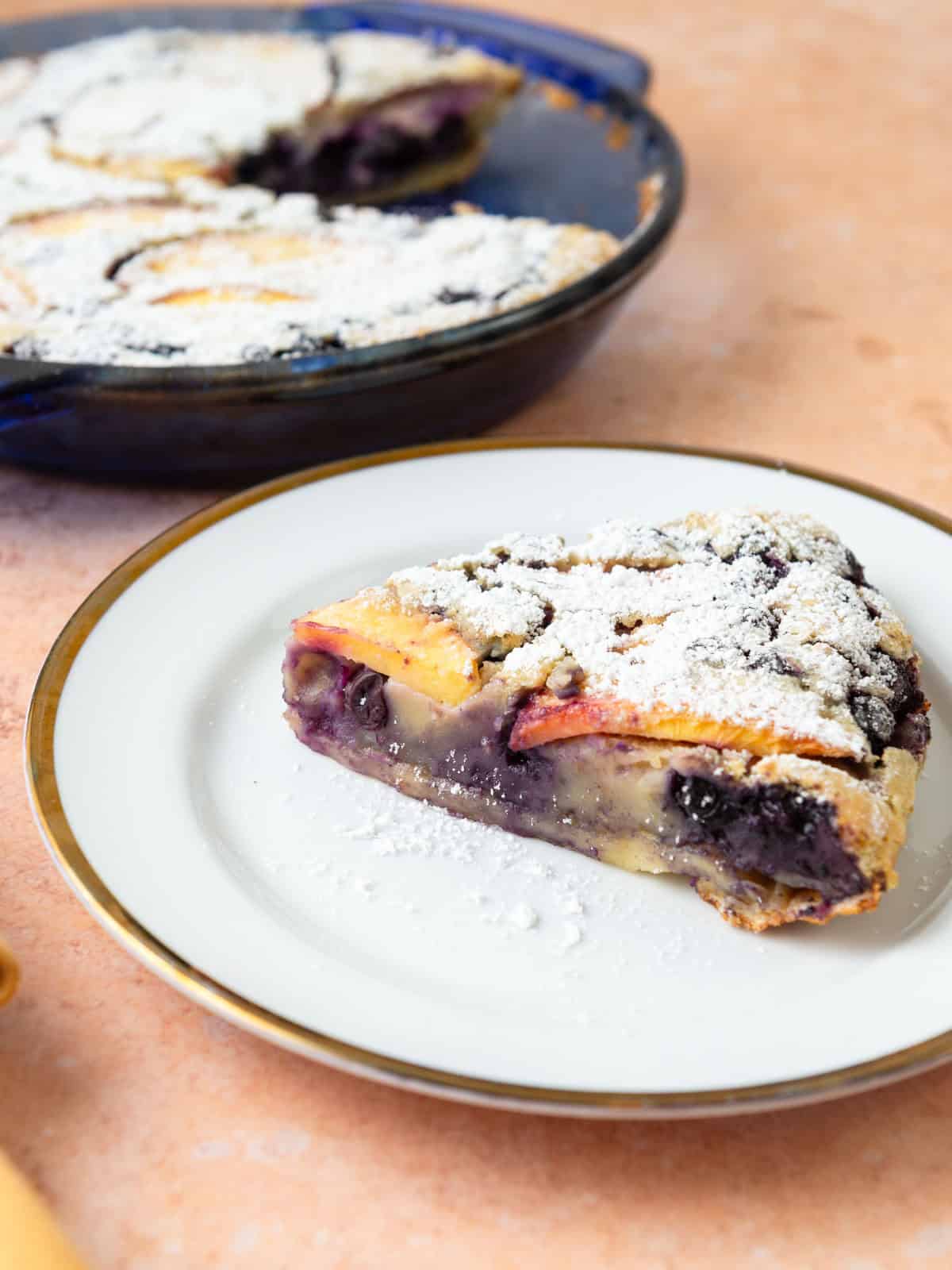 Peach and blueberry clafoutis is served with a light dusting of powdered sugar on top.