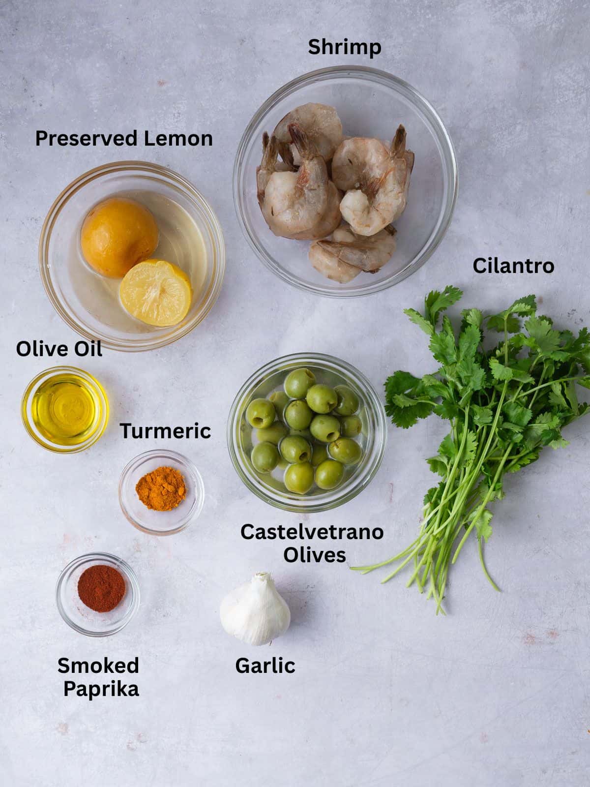 Ingredients for shrimp skewers including garlic, olive oil, spices and lemon and olives.