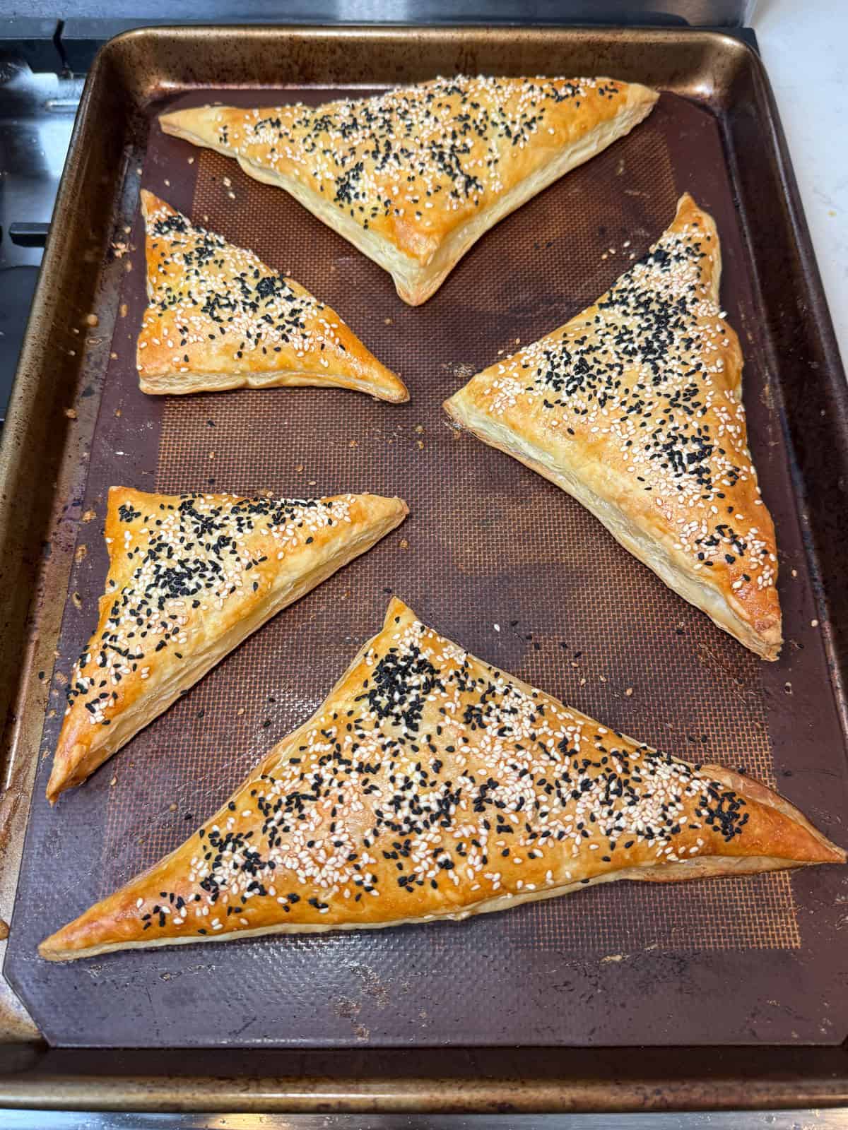 Cut the puff pastry into triangles, brush with egg wash and sprinkle of sesame seeds. Bake until golden and puffed up.