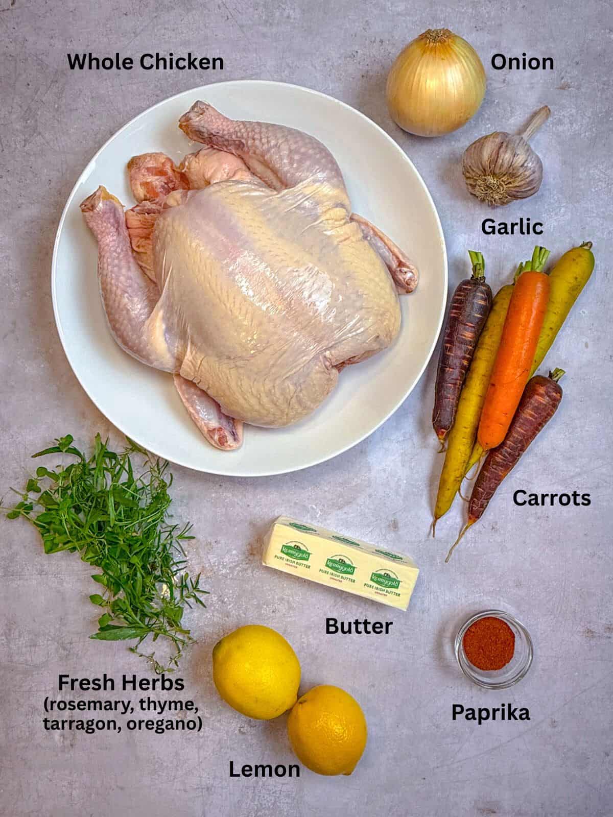 Ingredients for whole roasted chicken including carrots, onion, butter, lemon and herbs.