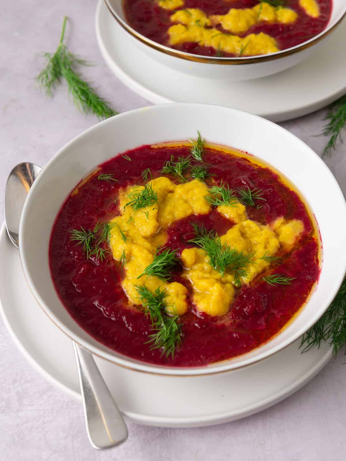 Red and yellow beet soup garnished with olive oil and fresh dill.