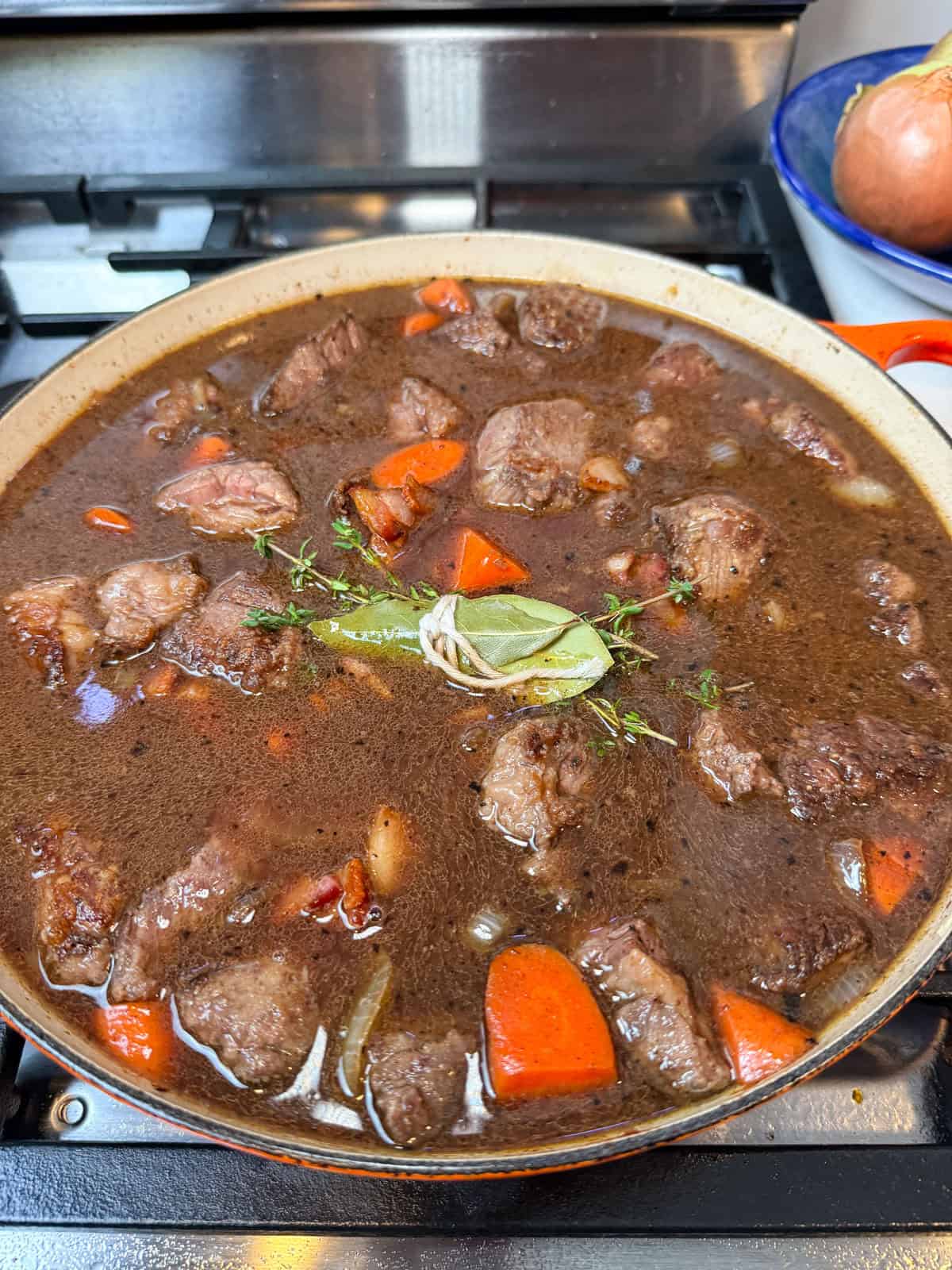 Add the beef, bacon, herbs, and broth back to the pot. Bring to a simmer, cover, and transfer to the oven to slow-braise until tender.