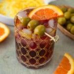This delicious lambrusco spritz cocktail is served with a salt and sugar rim and garnished with olives, olive oil and an orange slice.