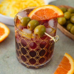 This delicious lambrusco spritz cocktail is served with a salt and sugar rim and garnished with olives, olive oil and an orange slice.