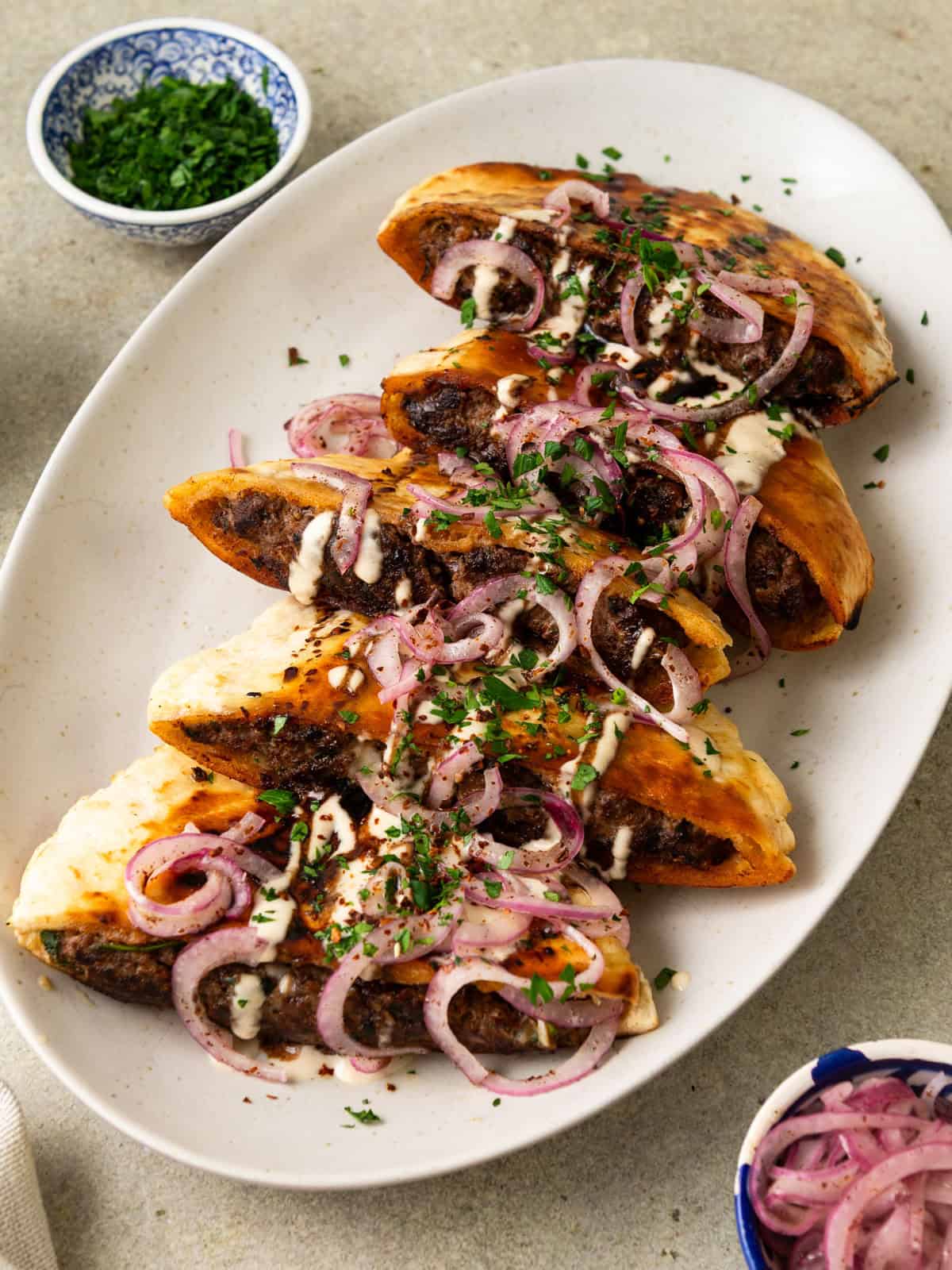 These beef arayes are pitas filled with a flavorful ground beef mixture. Once cooked, they are topped with pickled onions, tahini sauce and herbs.