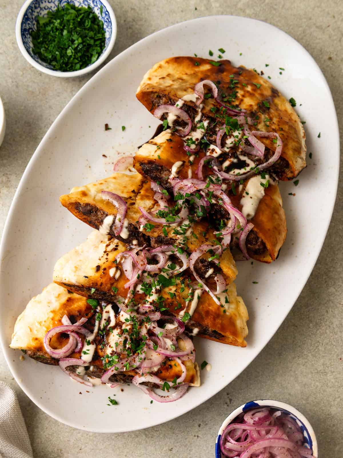 Middle Eastern beef arayes topped with pickled sumac onions, creamy tahini sauce and fresh herbs.
