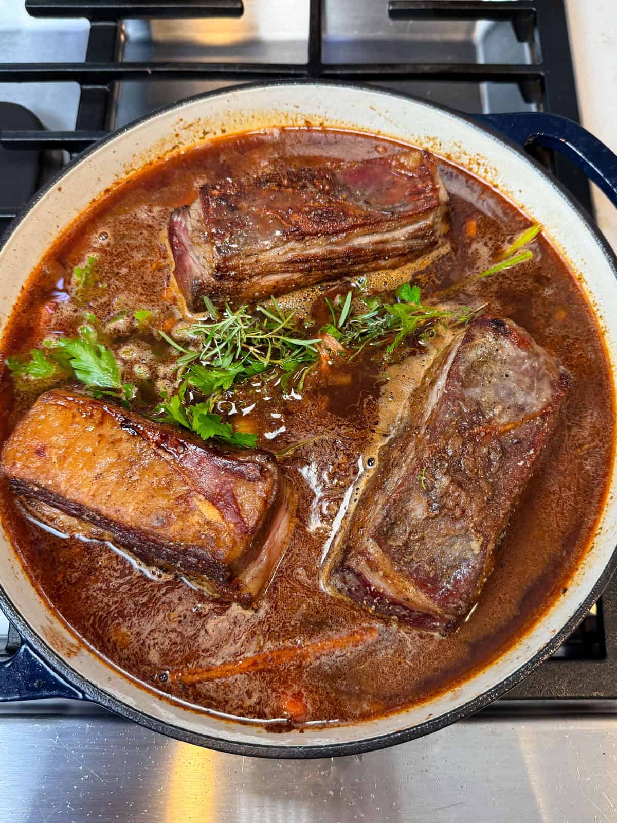 Nestle the seared short ribs back into the Dutch oven and add the braising liquid, red wine, pomegranate molasses and fresh herbs.