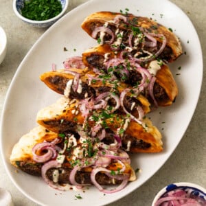 These Middle Eastern stuffed pitas are filled with a flavorful beef mixture and topped with sumac onions, creamy tahini sauce and herbs.