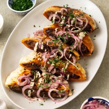 These Middle Eastern stuffed pitas are filled with a flavorful beef mixture and topped with sumac onions, creamy tahini sauce and herbs.