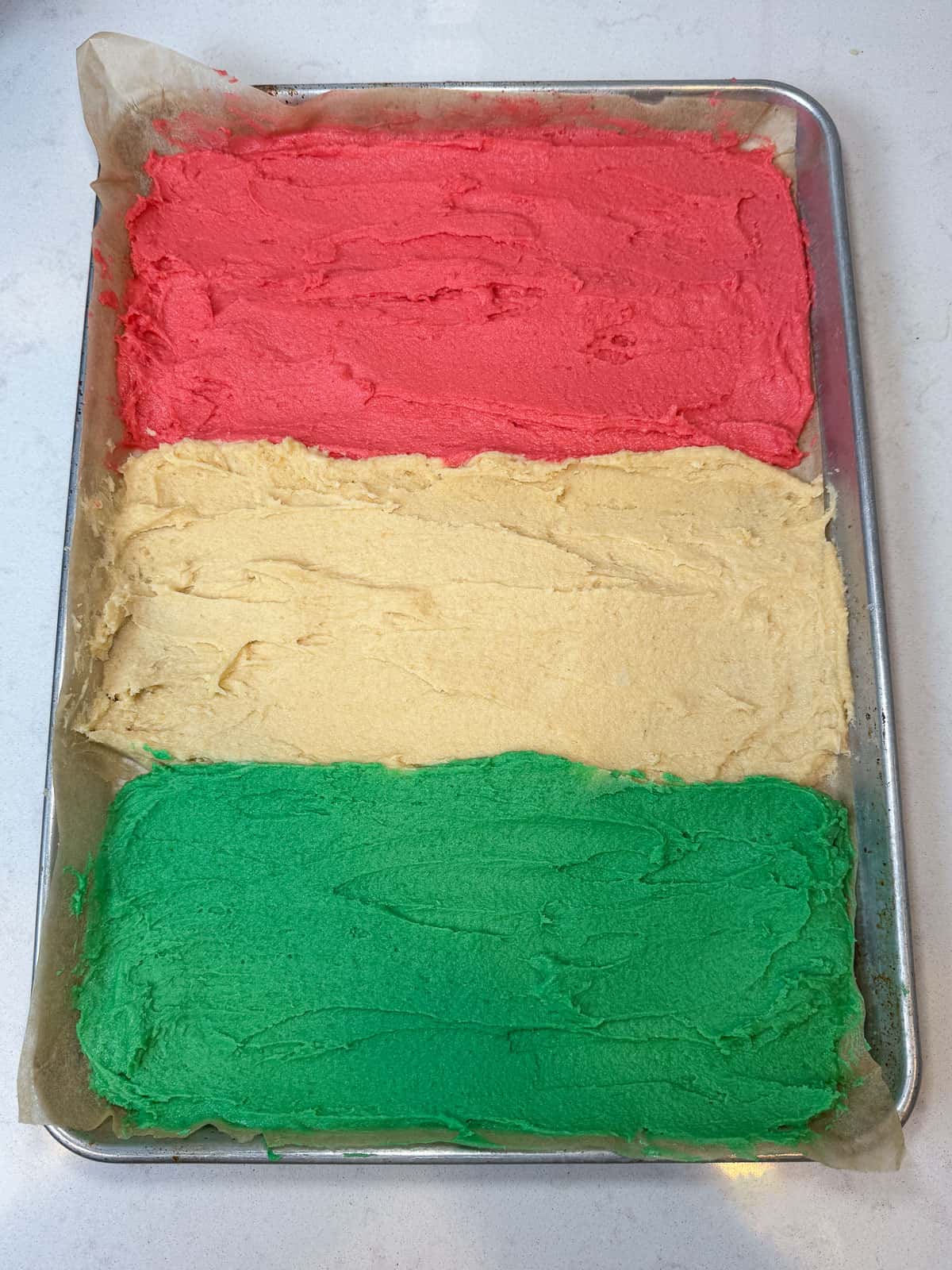 Divide a cookie sheet into three sections and spread the Italian rainbow cookie batters on the cookie sheet, keeping the colors separate.