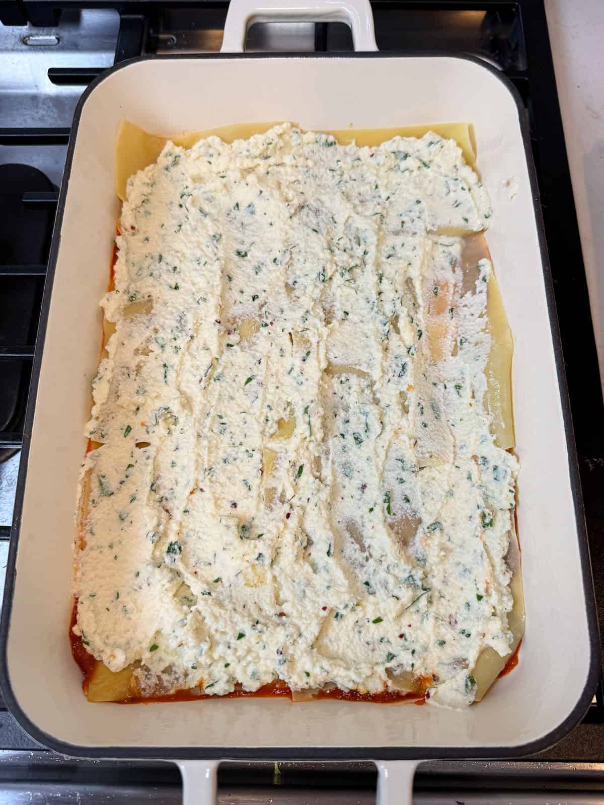 Spread a layer of ricotta on top of the cooked lasagna sheets for the vegetarian zucchini lasagna.
