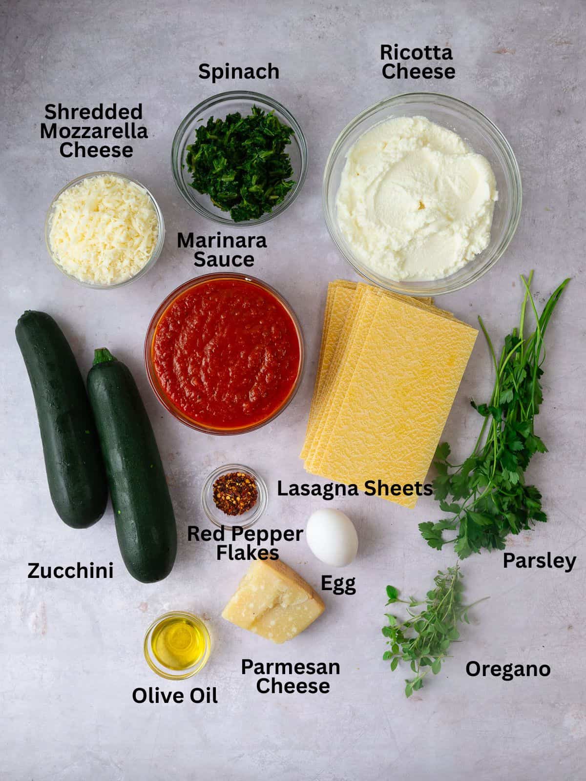 Ingredients for vegetarian zucchini lasagna, including lasagna sheets, spinach, mozzarella, ricotta and Parmesan cheese.