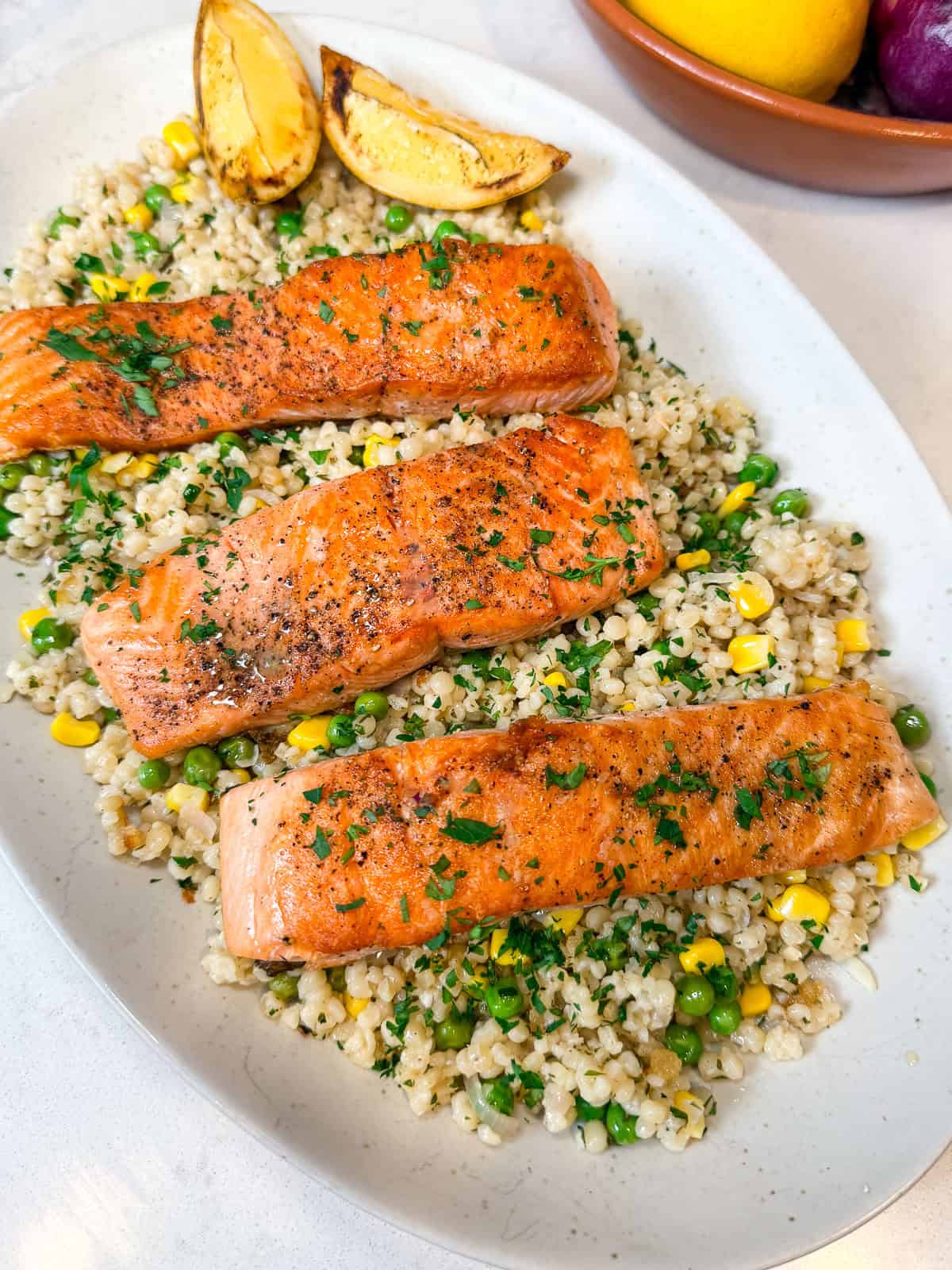 Serve the seared salmon over the pearl couscous with corn and peas.