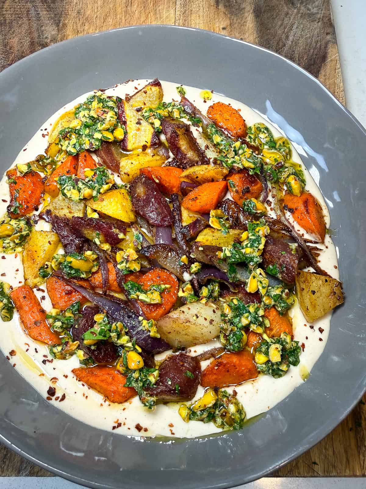 Spread a layer of creamy tahini sauce in a wide bowl and top with the roasted vegetables and garnish with the lemony pistachios gremolata.