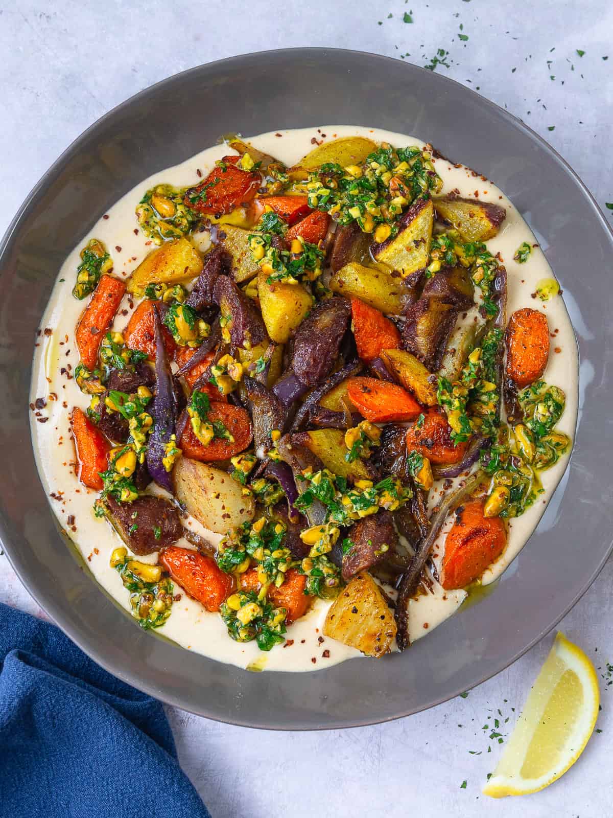 These savory roasted carrots are seasoned with warm spices and served over a lemony garlic tahini sauce and topped with herby pistachios.