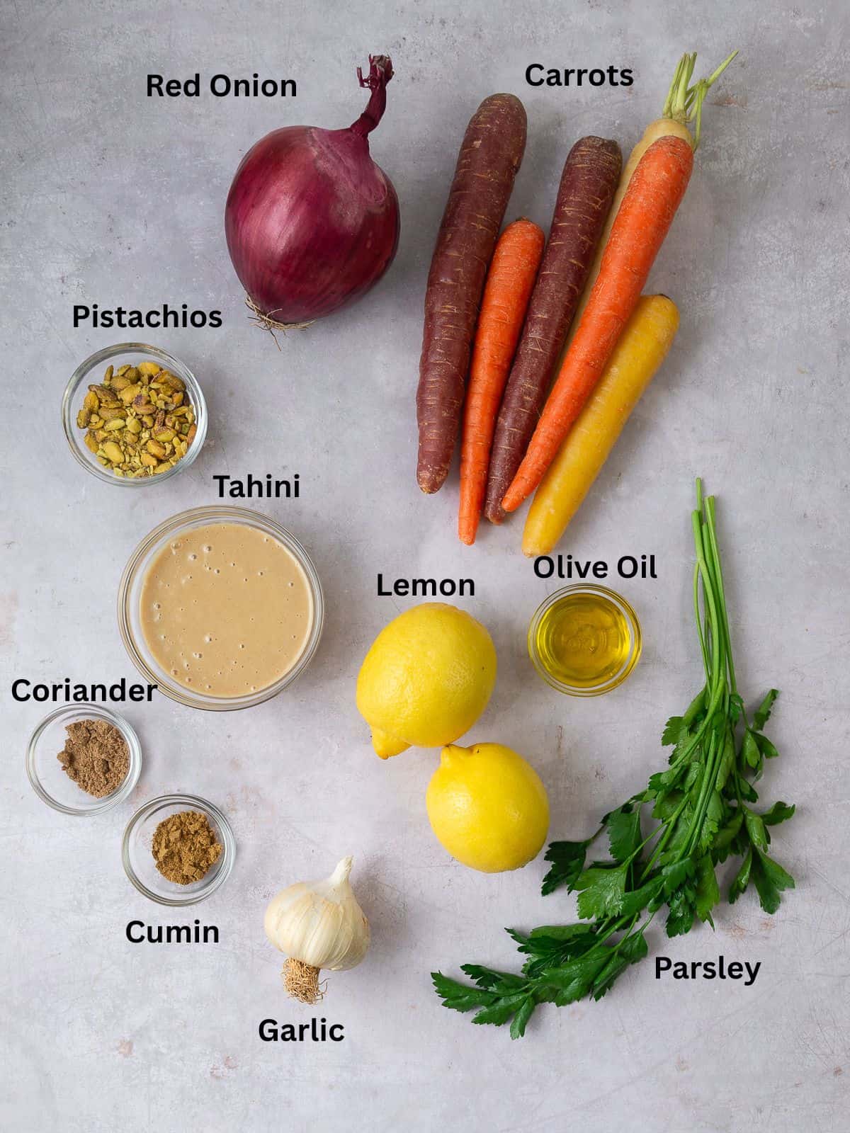 Ingredients for roasted carrots with tahini including pistachios, lemon, garlic, fresh herbs and spices.