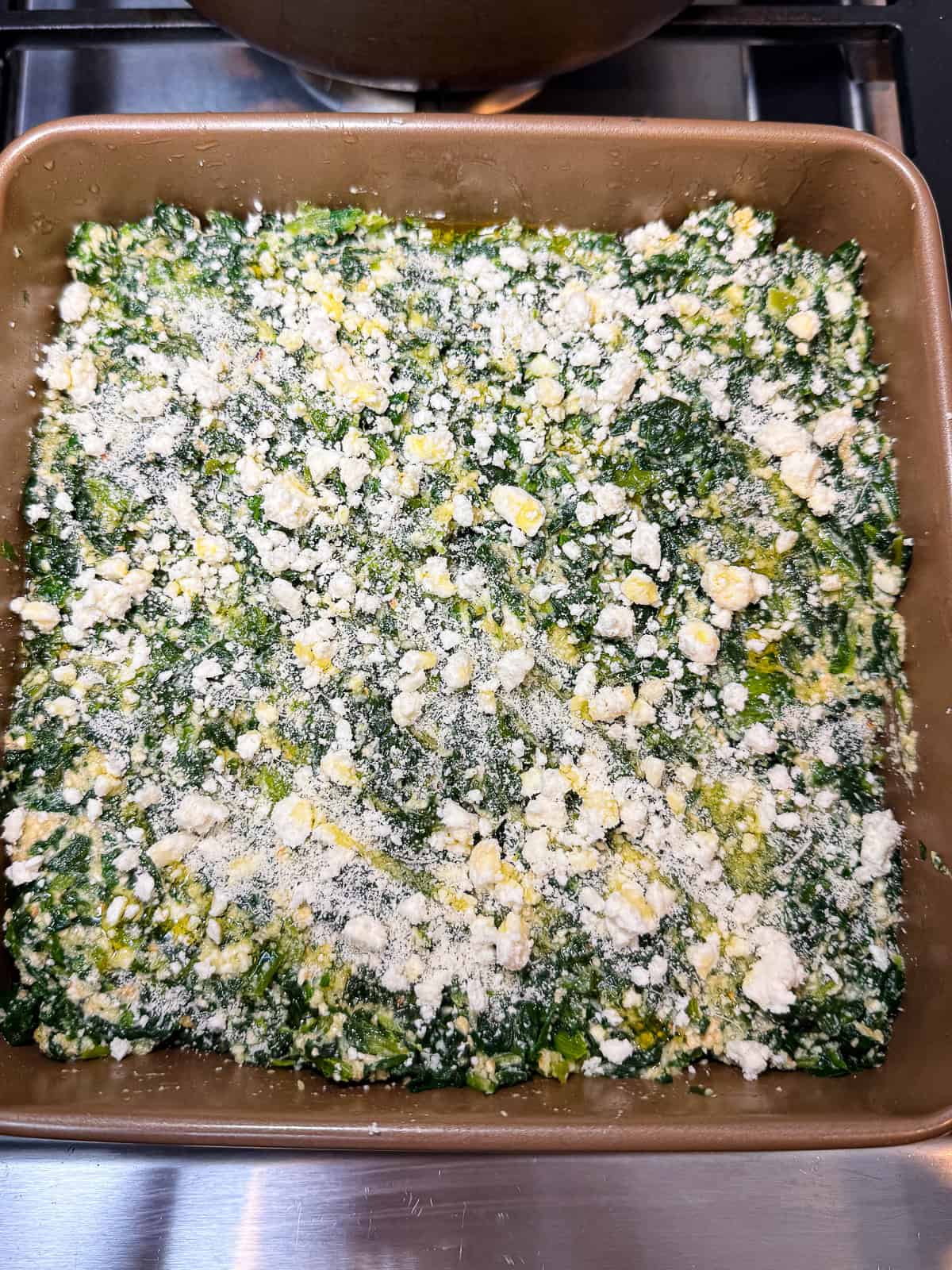 Transfer the spinach and cheese mixture to a square baking dish and to with crumbled feta, grated parmesan and drizzle of olive oil.