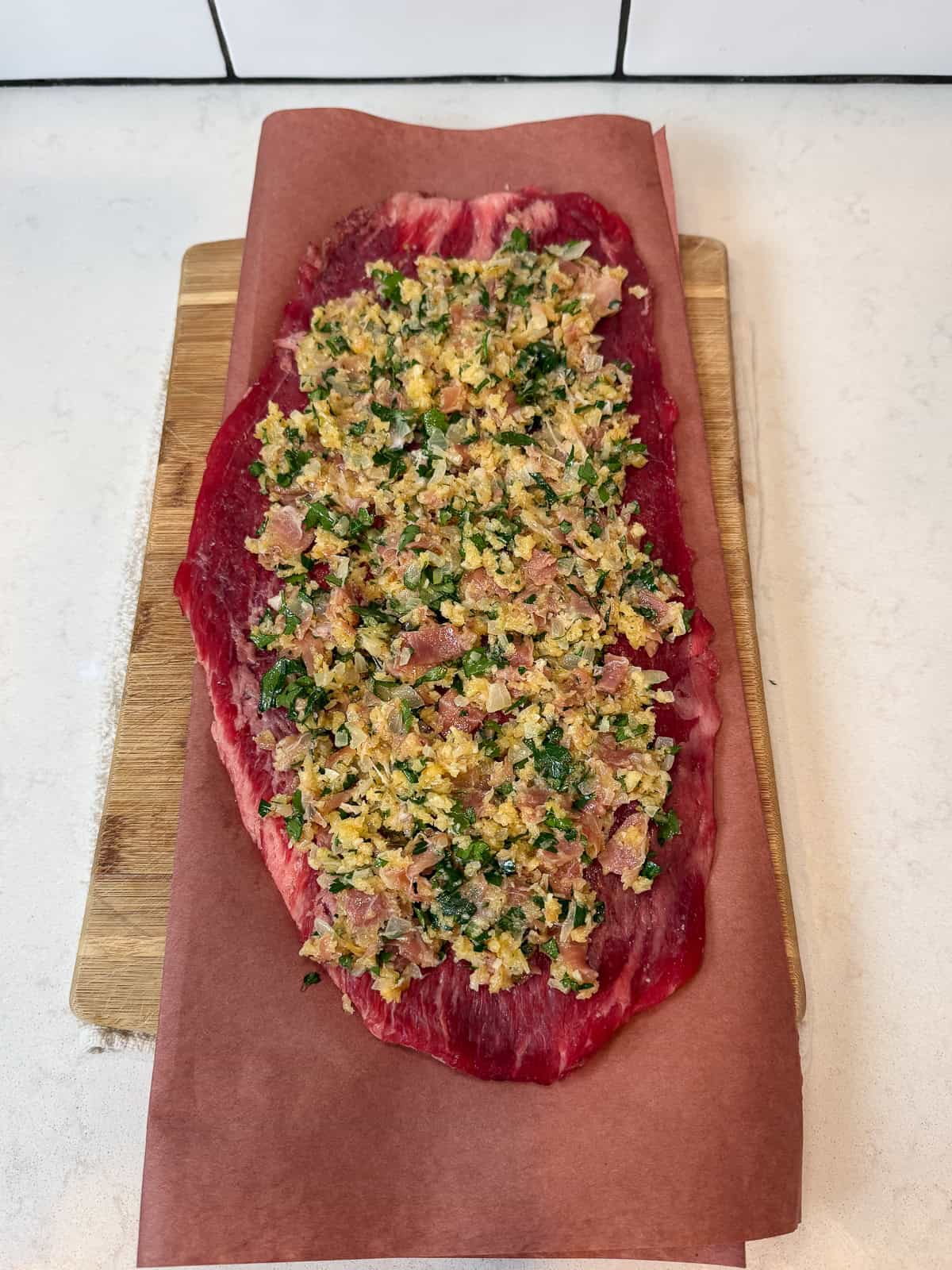 Spread the prosciutto and parmesan mixture onto the flattened flank steak.