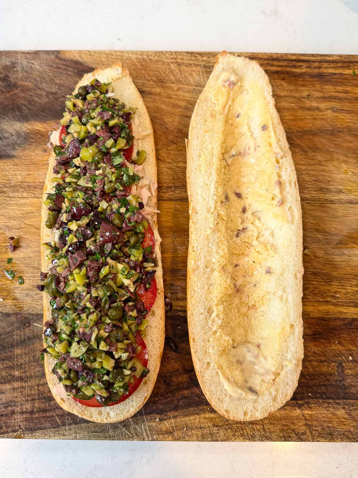 Spread the anchovy mayo on both sides of the bread and layer on the tuna, tomatoes and chopped olive salad.