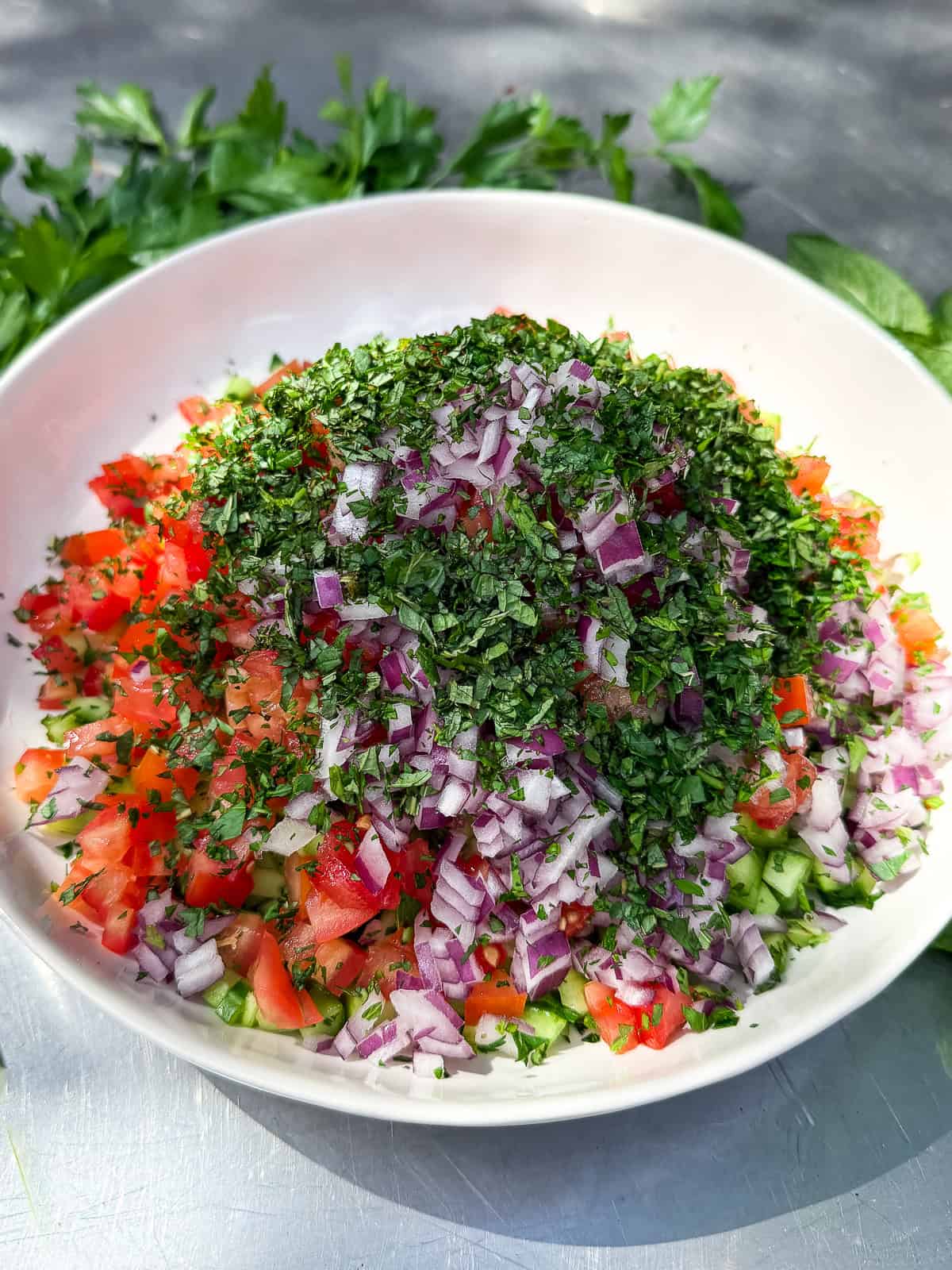 Add fresh parsley and mint to the chopped cucumber and tomato salad.