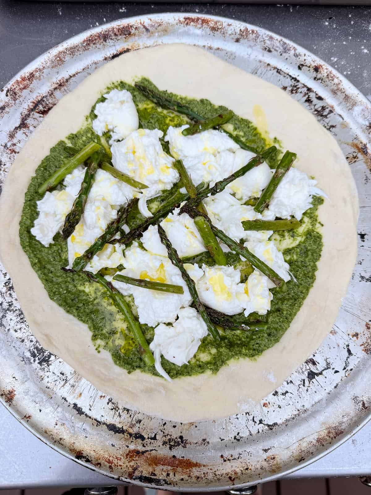 Layer the pizza dough with a thin layer of pesto, burrata and ricotta cheese and grilled asparagus.