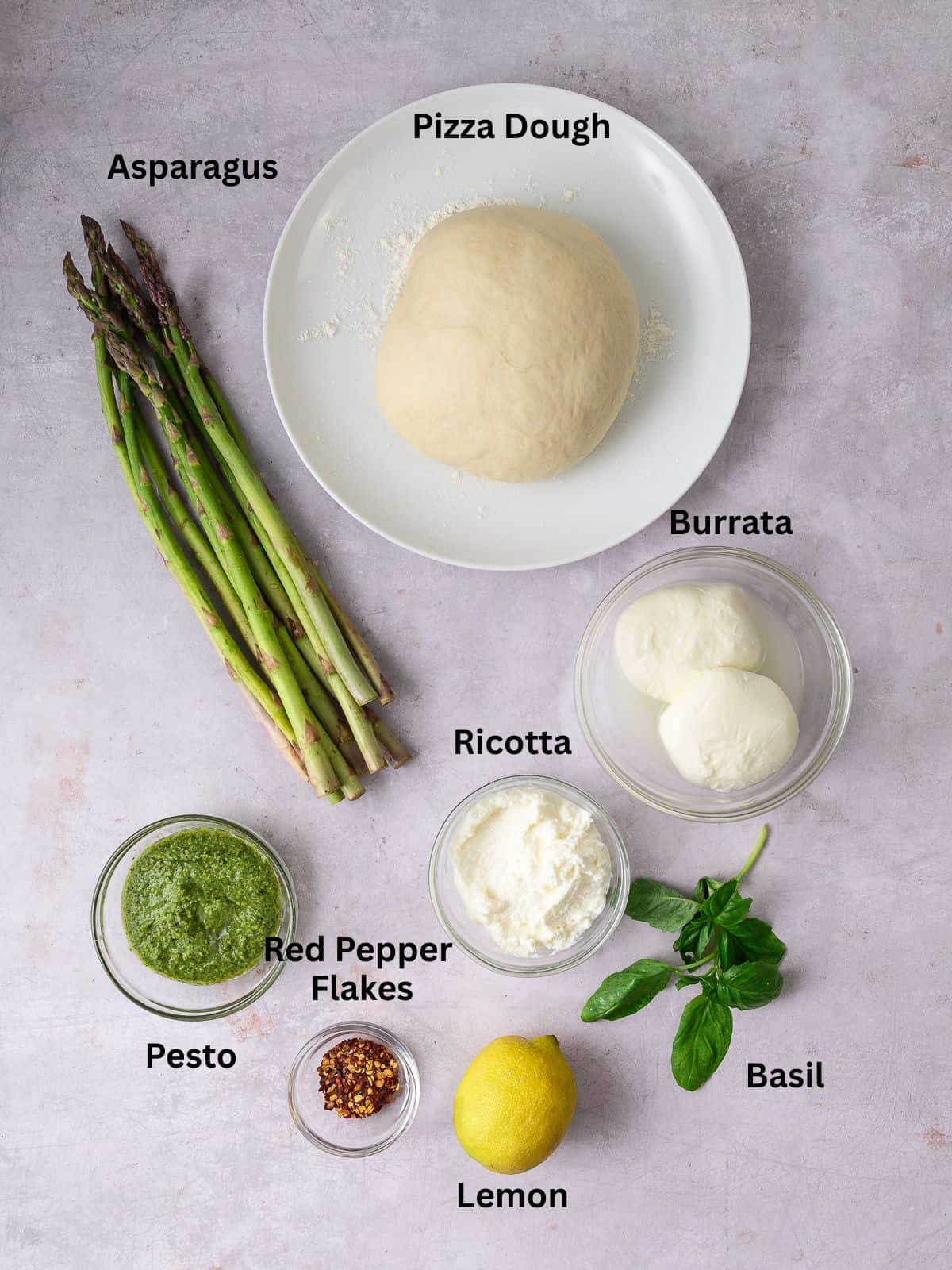 Ingredients for white pesto pizza, including ricotta, burrata, pesto and asparagus.