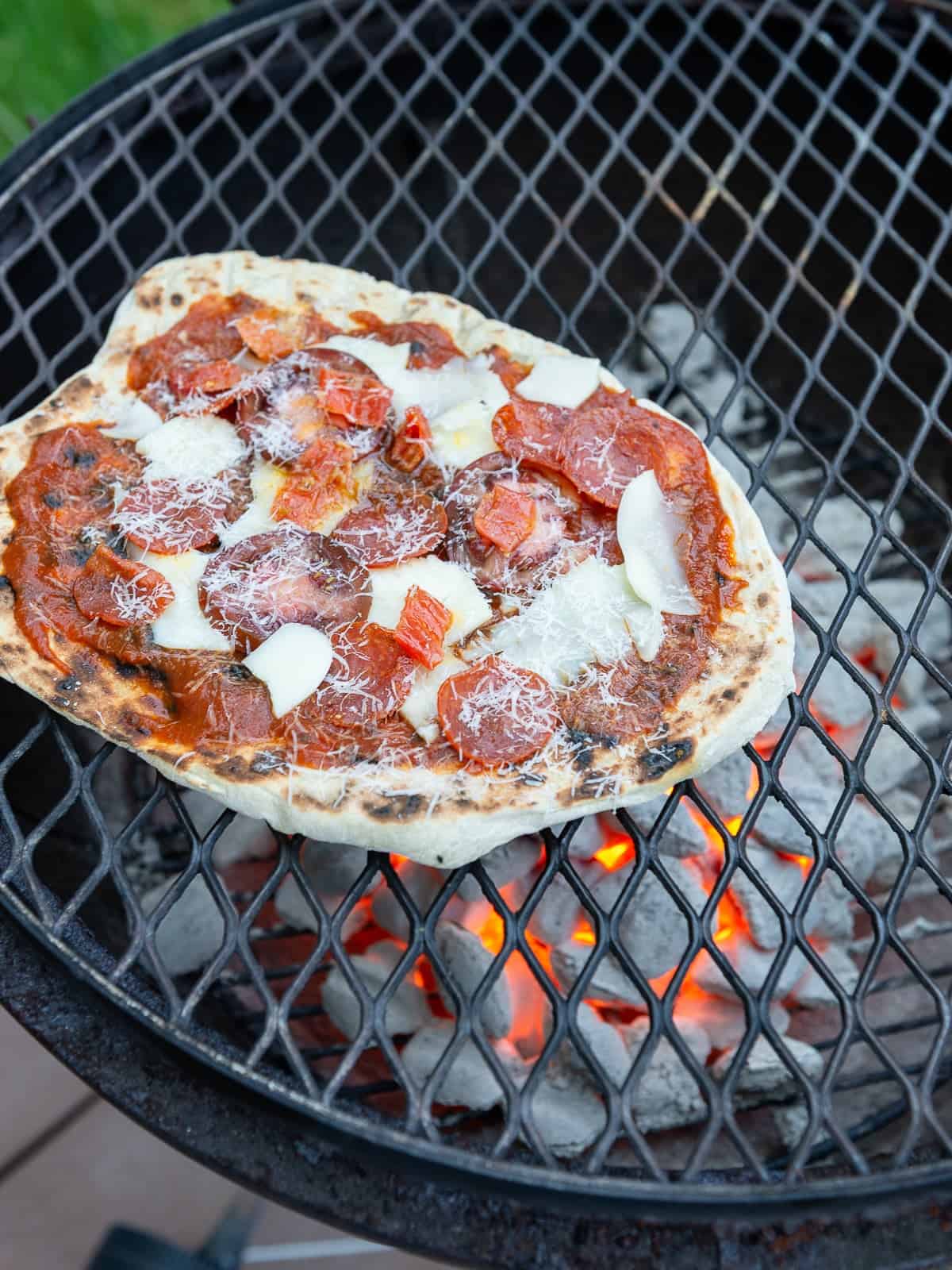 Cook the topped pizza on the grill until the cheese melts and cover the grill if needed.