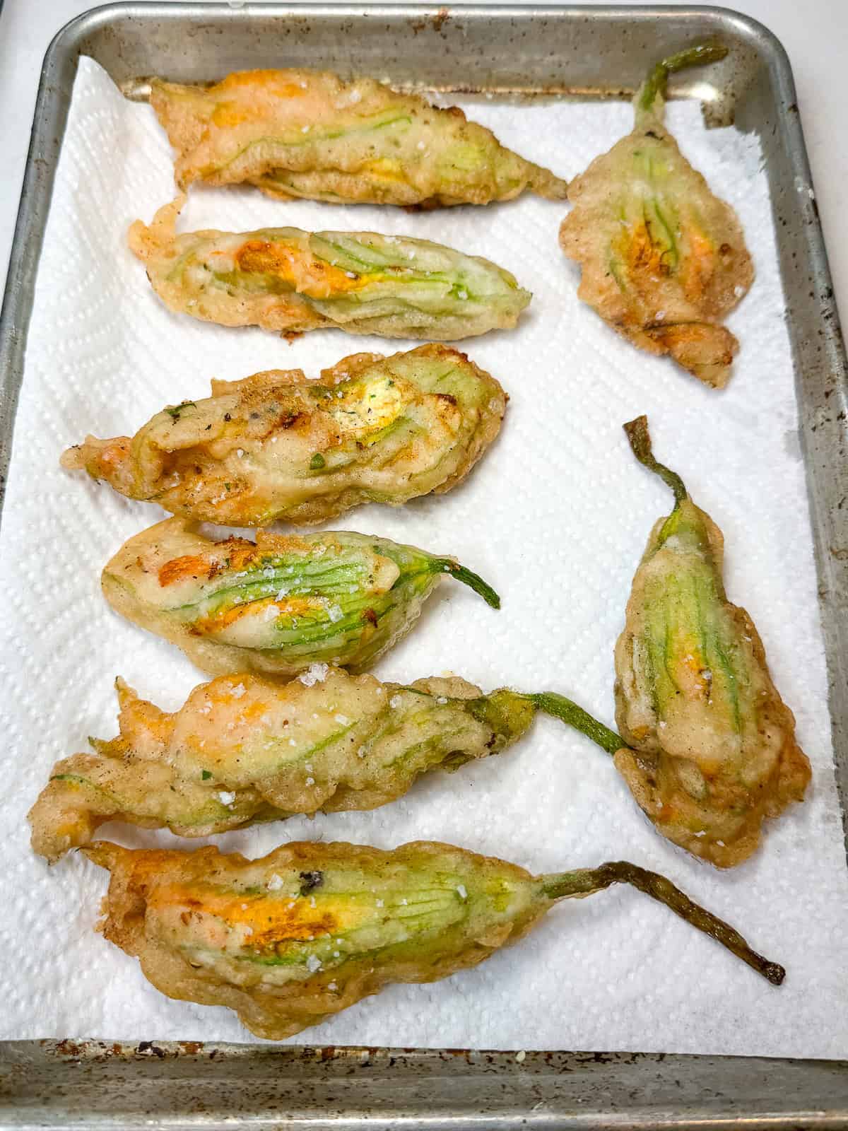 Lay the fried stuffed squash blossoms on a paper towel lined baking sheet to drain excess oil.