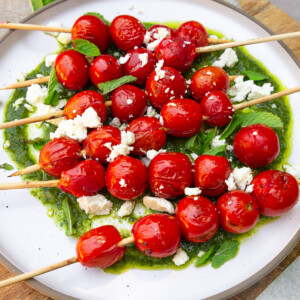 Grilled cherry tomatoes are served on top of a vibrant herb vinaigrette and finished with feta cheese and fresh mint.