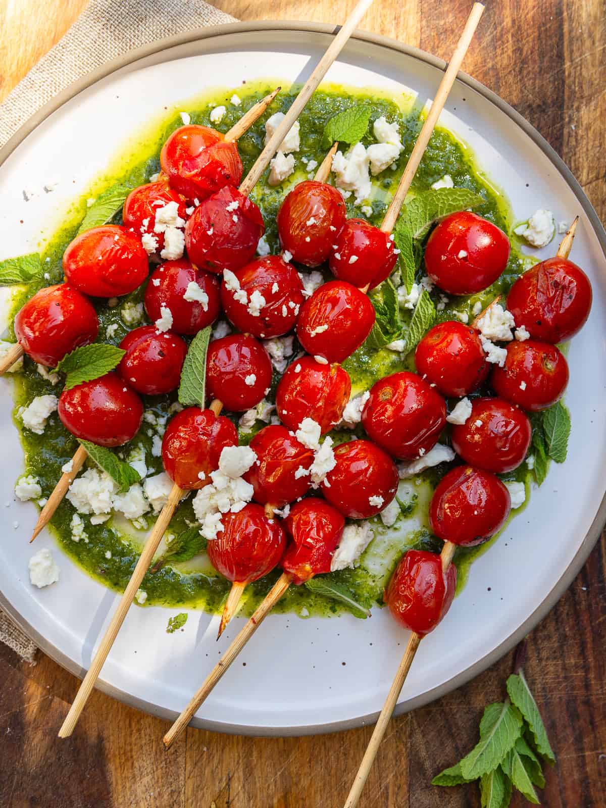 Grilled cherry tomato skewers are layered on top of a fresh herb vinaigrette and garnished with crumbled feta cheese.
