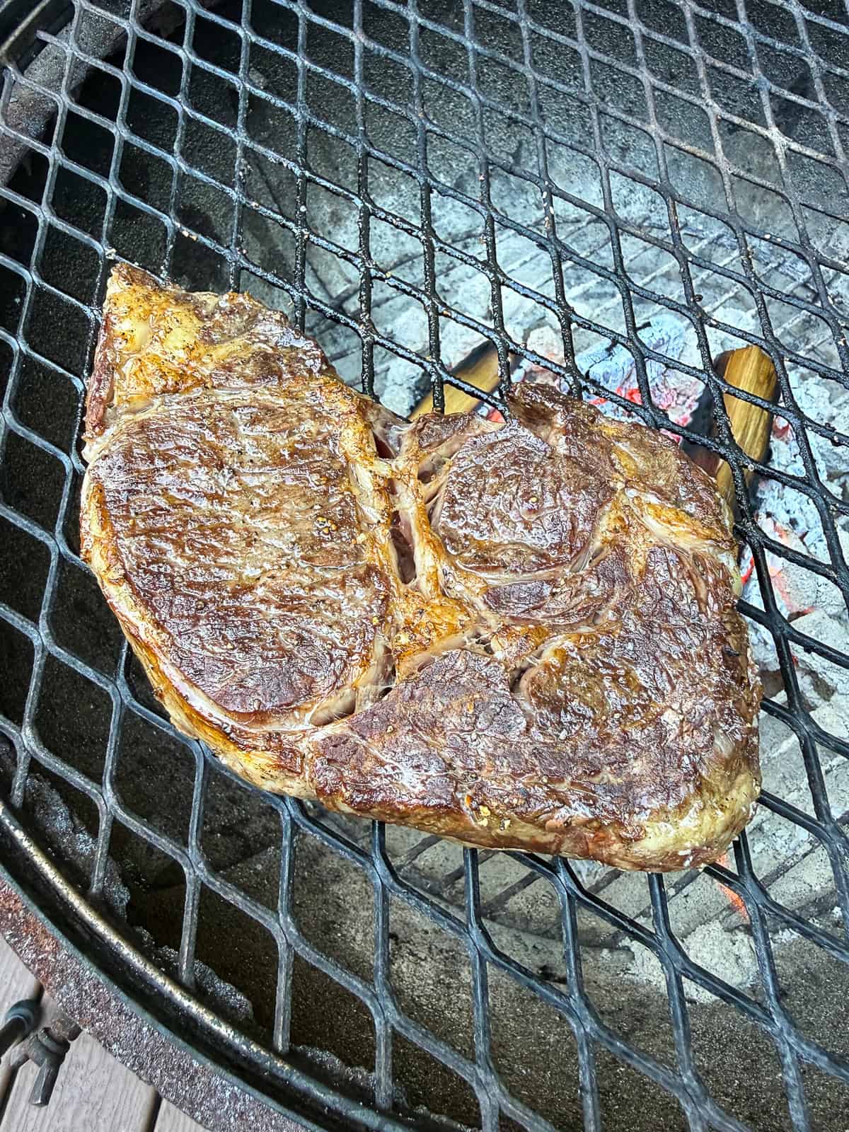 Grill the ribeye steak on a charcoal grill until charred on the outside and medium rare in the center.