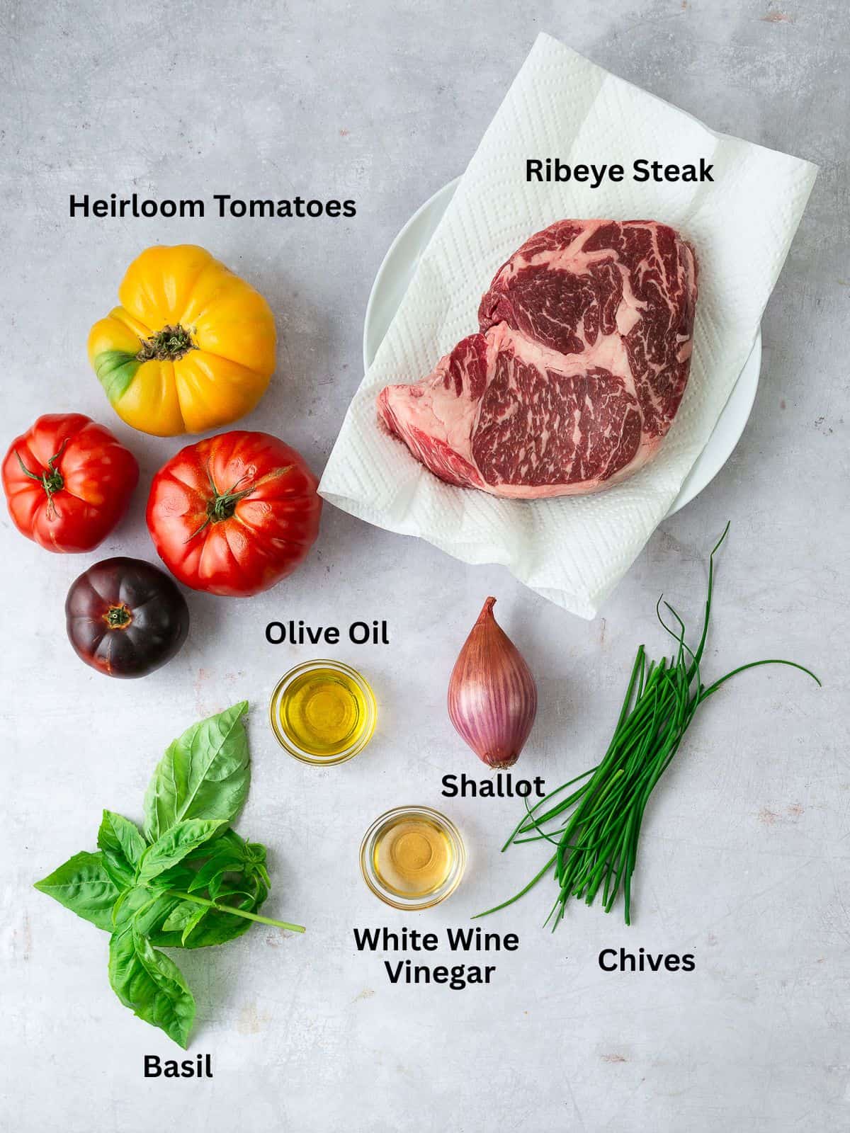Ingredients for ribeye steak salad with heirloom tomatoes, shllot, fresh herbs and olive oil and vinegar.