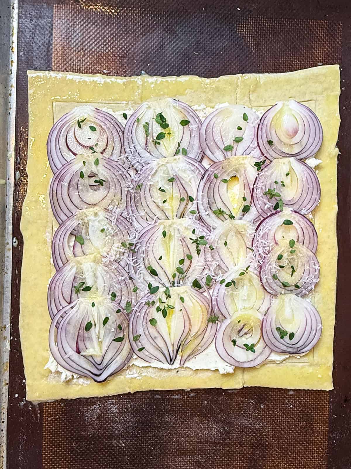 Layer the sliced onions over the boursin cheese and top with fresh thyme and parmesan cheese before baking.